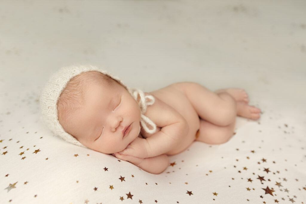 Sleeping newborn wearing a white bonnet on a star blanket.