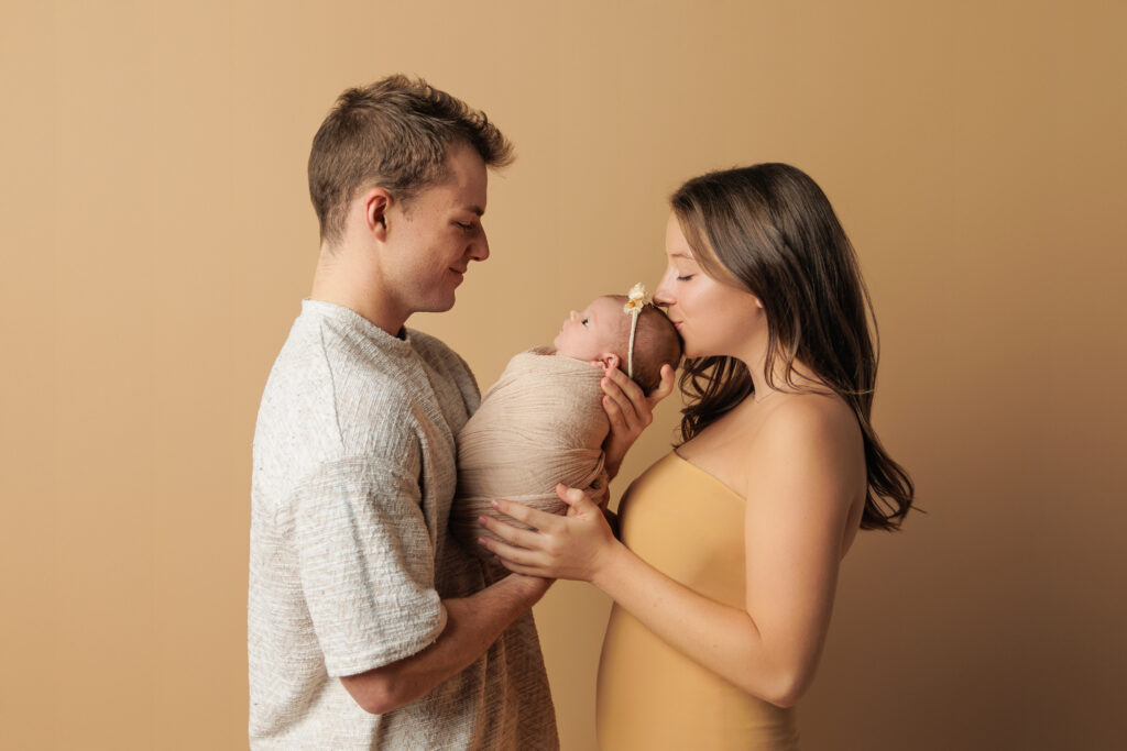 Parents sharing a kiss with their newborn baby during a studio session with Charlottesville newborn photographer.