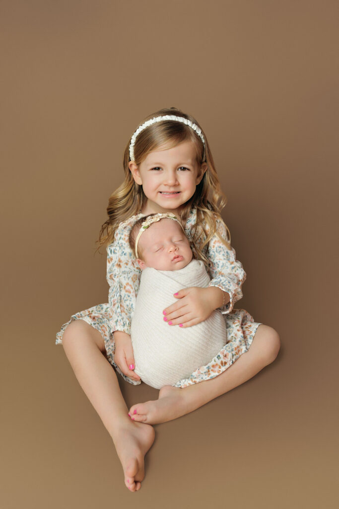 Big sister holding her newborn sibling during a Charlottesville newborn photography session.