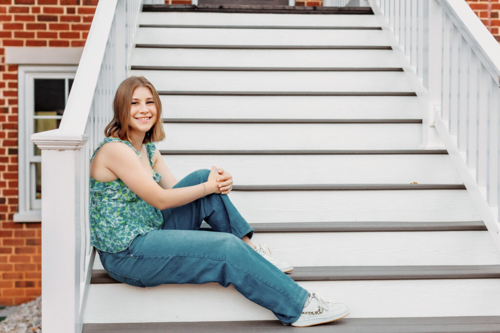 High school senior sitting on white outdoor steps in a casual outfit during a multiple locations senior photos session with Amy Yang Photography.
