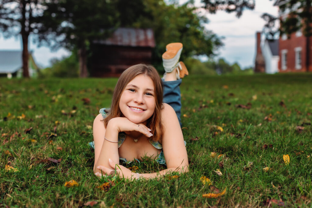 High school senior lying on green grass and smiling in front of historic buildings during a fun senior photos in Charlottesville, VA.