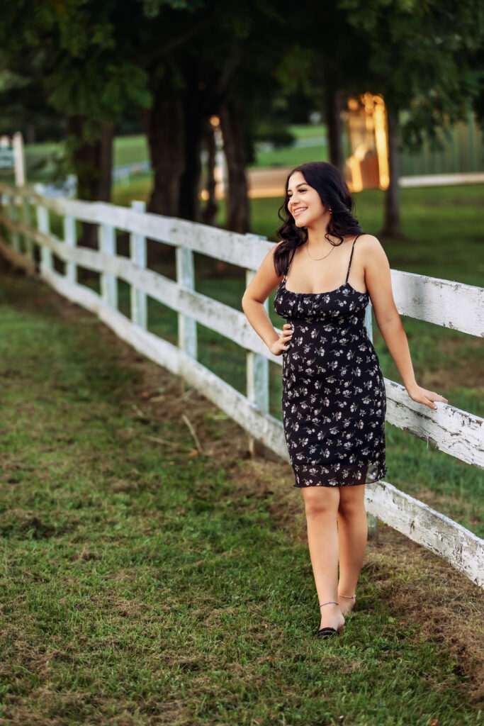 Smiling high school senior sitting on a white wooden fence during a golden hour outdoor senior portrait session in Charlottesville, VA.