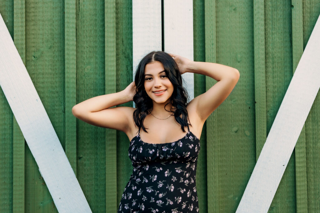 Smiling high school senior posing in front of green barn doors during a relaxed outdoor senior photography session in Charlottesville, VA.